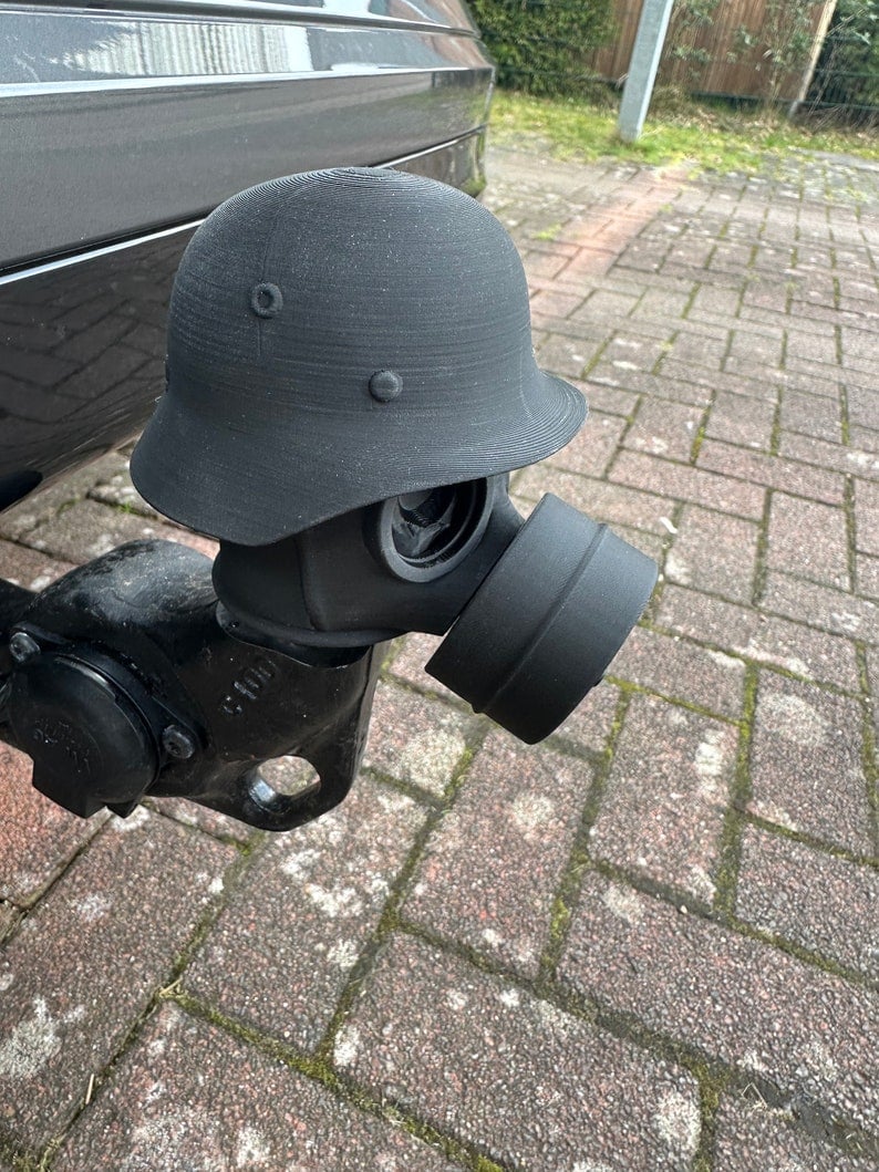 May include: A black gas mask attached to a black helmet. The helmet has a round shape with a brim and is attached to the gas mask with a black fabric covering the connection. The gas mask has a round filter attached to the front. May include: A black gas mask attached to a black helmet. The helmet has a round shape with a brim and is attached to the gas mask with a black fabric covering the connection. The gas mask has a round filter attached to the front.